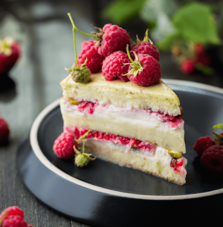 A raspberry layer cake slice with fresh raspberries on top server on a fancy plate.